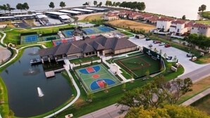 Ein Luftbild eines Wohngebiets mit mehreren Tennisplätzen, einem Schwimmbad und Häusern mit roten Ziegeldächern.