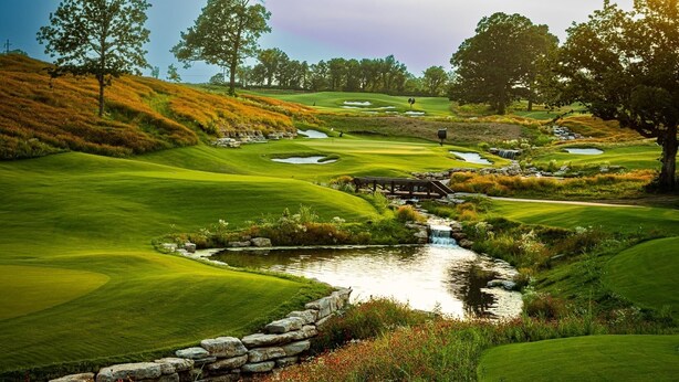 Ein Golfplatz mit Teich, Steinmauern und Bäumen.