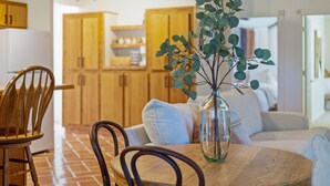 Ein Essbereich mit einem runden Holztisch, zwei Stühlen und einer Vase mit grünen Blättern.
