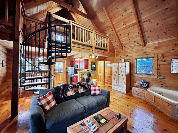A cozy cabin interior with a spiral staircase, a living room with a sofa and a dog, a kitchen area, and a bathroom with a bathtub.