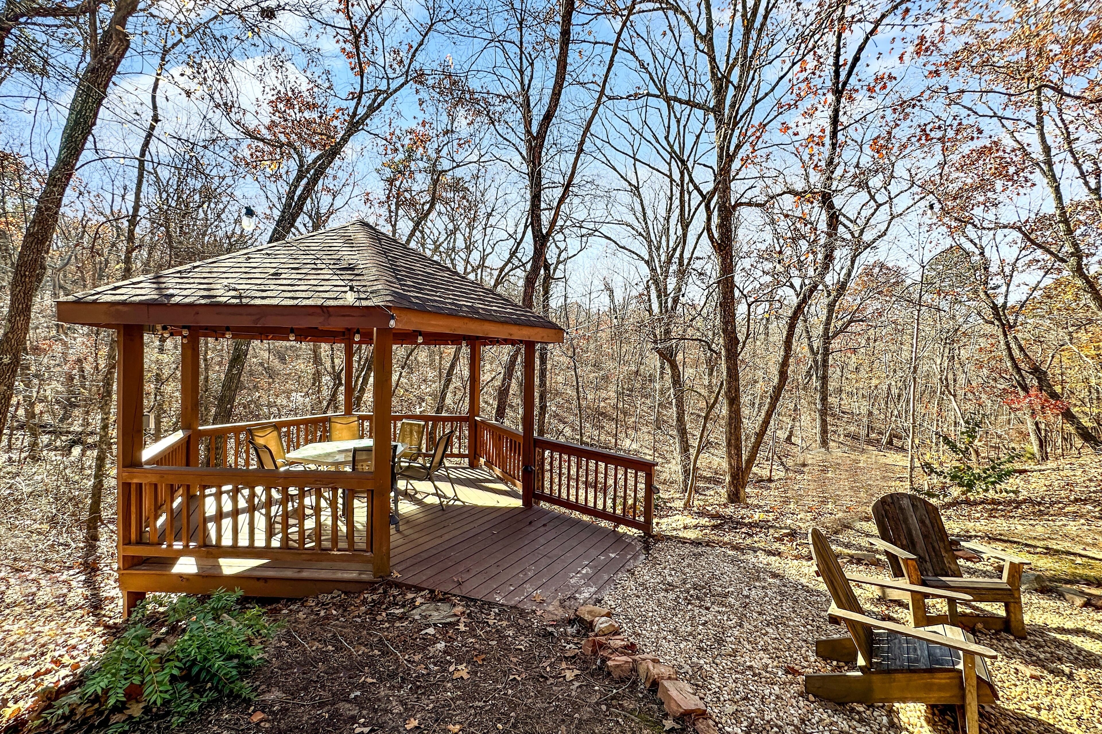 A wooden gazebo with a bench and a chair in a forest setting.