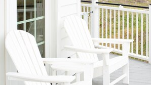 Eine weiße Holzveranda mit zwei Adirondack-Stühlen und einem weißen Geländer.