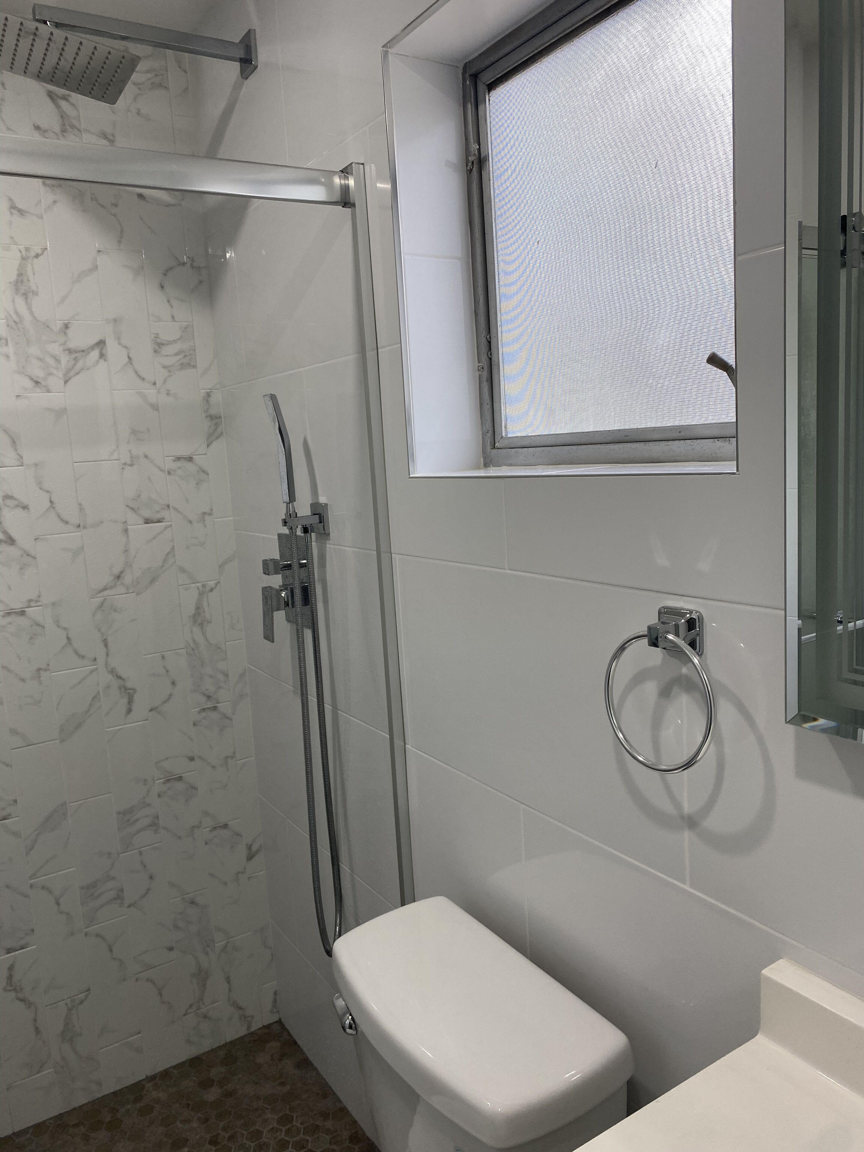Ein Badezimmer mit Duschkabine aus Glas, Toilette und Fenster.