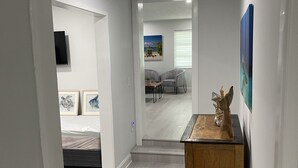 Ein moderner, gut beleuchteter Flur mit einem Holztisch, einem Bett mit weißer Matratze und einem Gemälde mit Strandmotiv an der Wand.