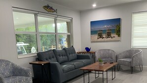 Ein modernes Wohnzimmer mit einem grauen Sofa, zwei Sesseln, einem Couchtisch und einem Gemälde einer Strandansicht.