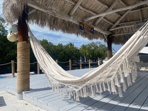 Una hamaca bajo una estructura de techo de paja con un letrero que dice "Solo otro día en el paraíso."