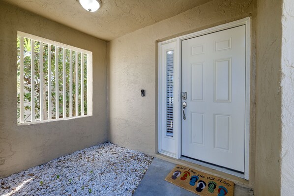 A room with a white door, a window with vertical blinds, and a doormat with a peace symbol.