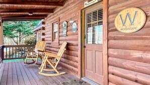 A wooden cabin with a porch, rocking chairs, and a welcome sign.