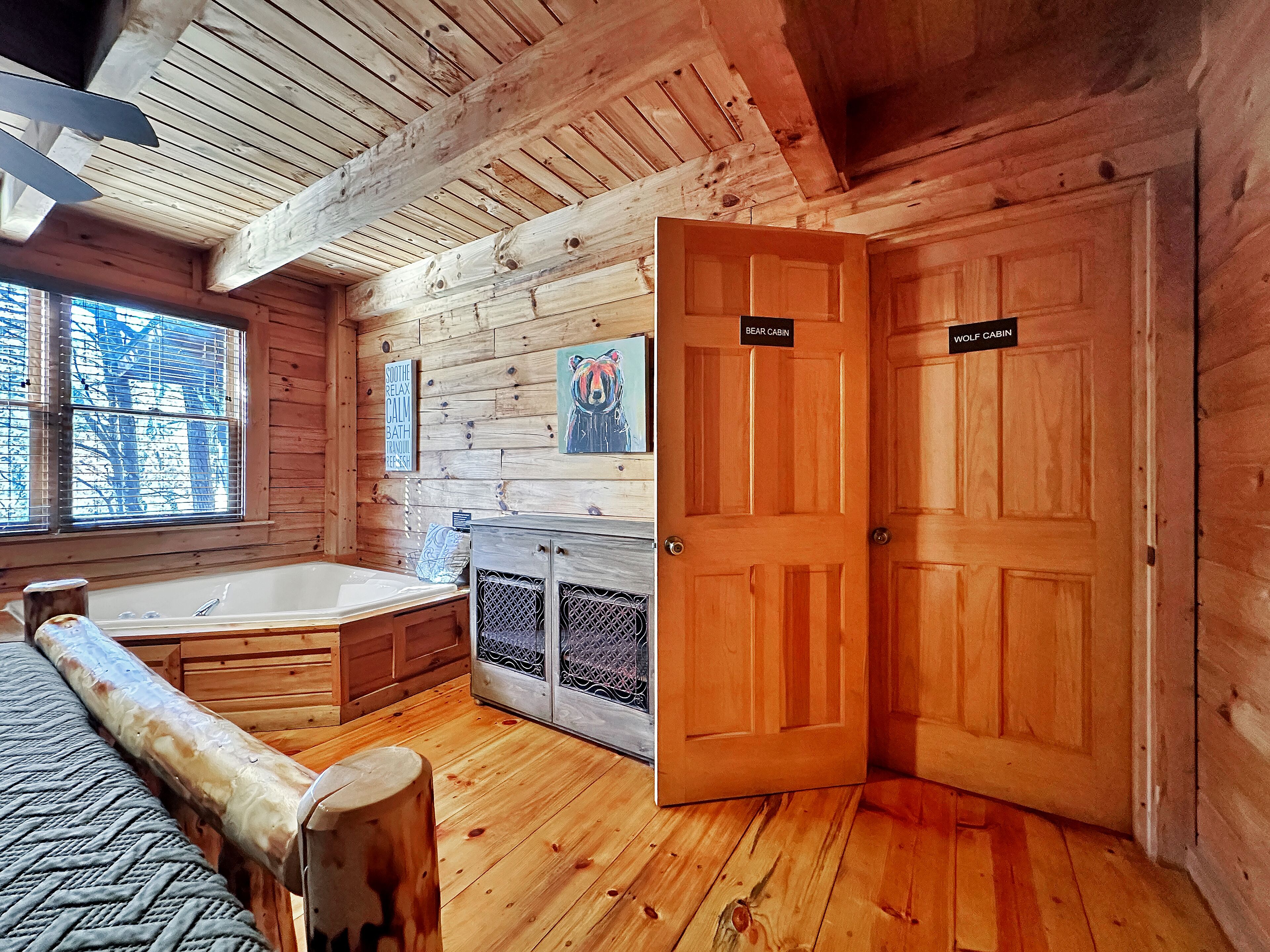L’intérieur d’un chalet avec un plancher en bois, une baignoire, une œuvre d’art sur le thème des ours et deux portes portant les inscriptions suivantes : « Chalet de l’Ours » et « Chalet du Loup ».