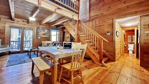 A wooden cabin interior with a dining area, a staircase, and a bathroom.