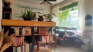 A cozy living room with a bookshelf, a sofa, and a coffee table. There are several potted plants and a ceiling fan. - Nanxi Longevity Flower Farmer Stay Inn (Yongjia)