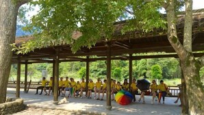 A covered outdoor seating area with stone flooring, surrounded by trees and a view of greenery. - Nanxi Longevity Flower Farmer Stay Inn (Yongjia)