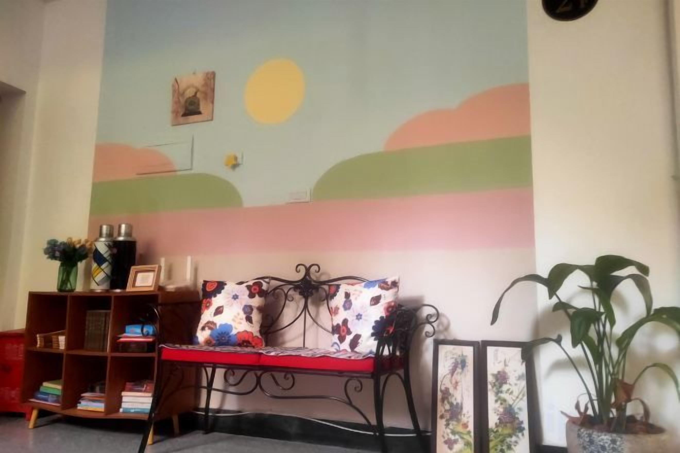 A room with a sofa, a bookshelf, and a wall with a painted landscape.