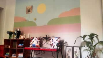 A room with a sofa, a bookshelf, and a wall with a painted landscape.