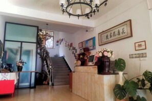 A reception area with a staircase, a reception desk, and a wall with framed pictures and a sign. - Nanxi Longevity Flower Farmer Stay Inn (Yongjia)