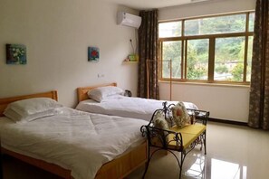 A room with two beds, a table with a vase, a window with curtains, and a wall-mounted air conditioner. - Nanxi Longevity Flower Farmer Stay Inn (Yongjia)