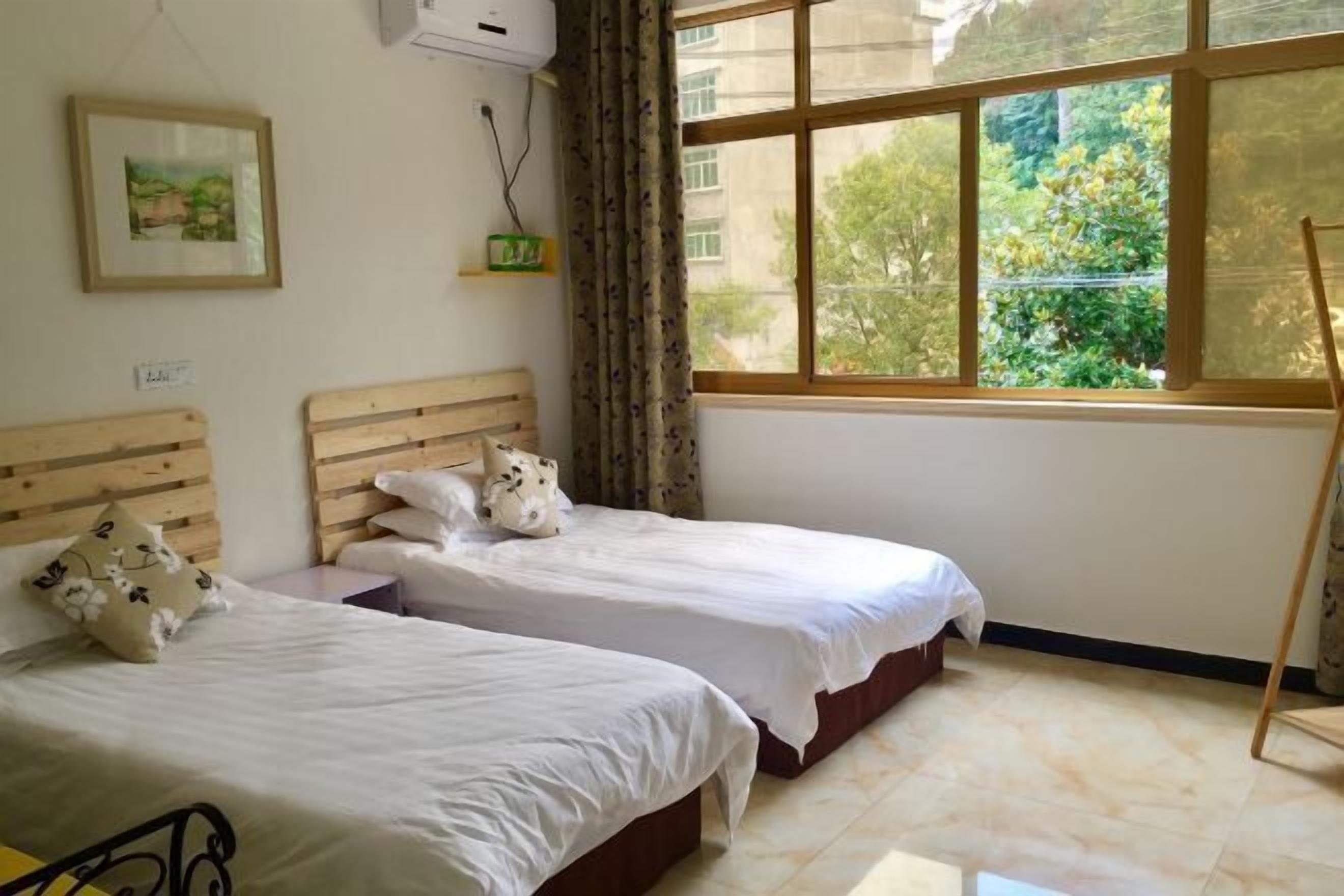 Quarto com duas camas, janela com vista para o verde e cabeceira de madeira.