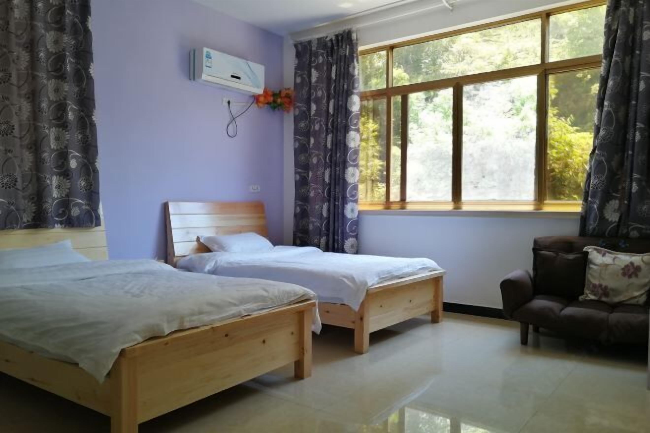 Una habitación con dos camas de madera, un sofá, una ventana con cortinas y un equipo de aire acondicionado.