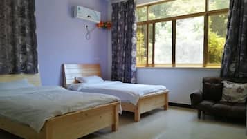 Una habitación con dos camas de madera, un sofá, una ventana con cortinas y un equipo de aire acondicionado.