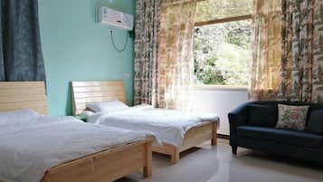 Una habitación con dos camas de madera, un sofá oscuro y una ventana con cortinas florales.