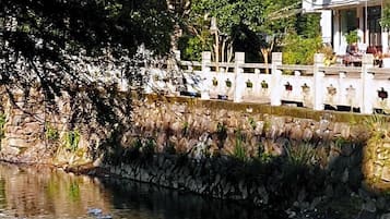 Un muro de piedra con una cerca blanca, una masa de agua con patos, y un edificio con balcón al fondo.