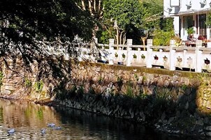 A stone wall with a white fence, a body of water with ducks, and a building with a balcony in the background.