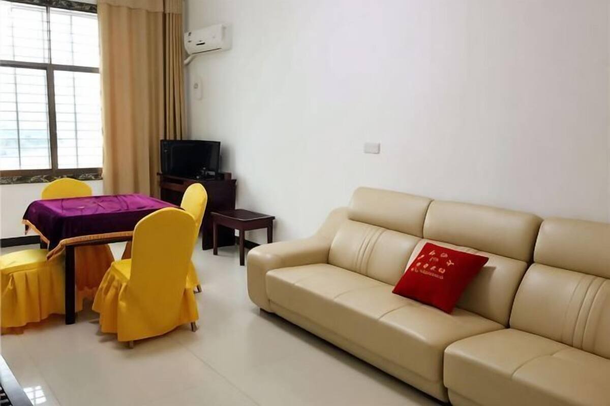 A living room with a beige sofa, yellow chairs, a small table, and a television.