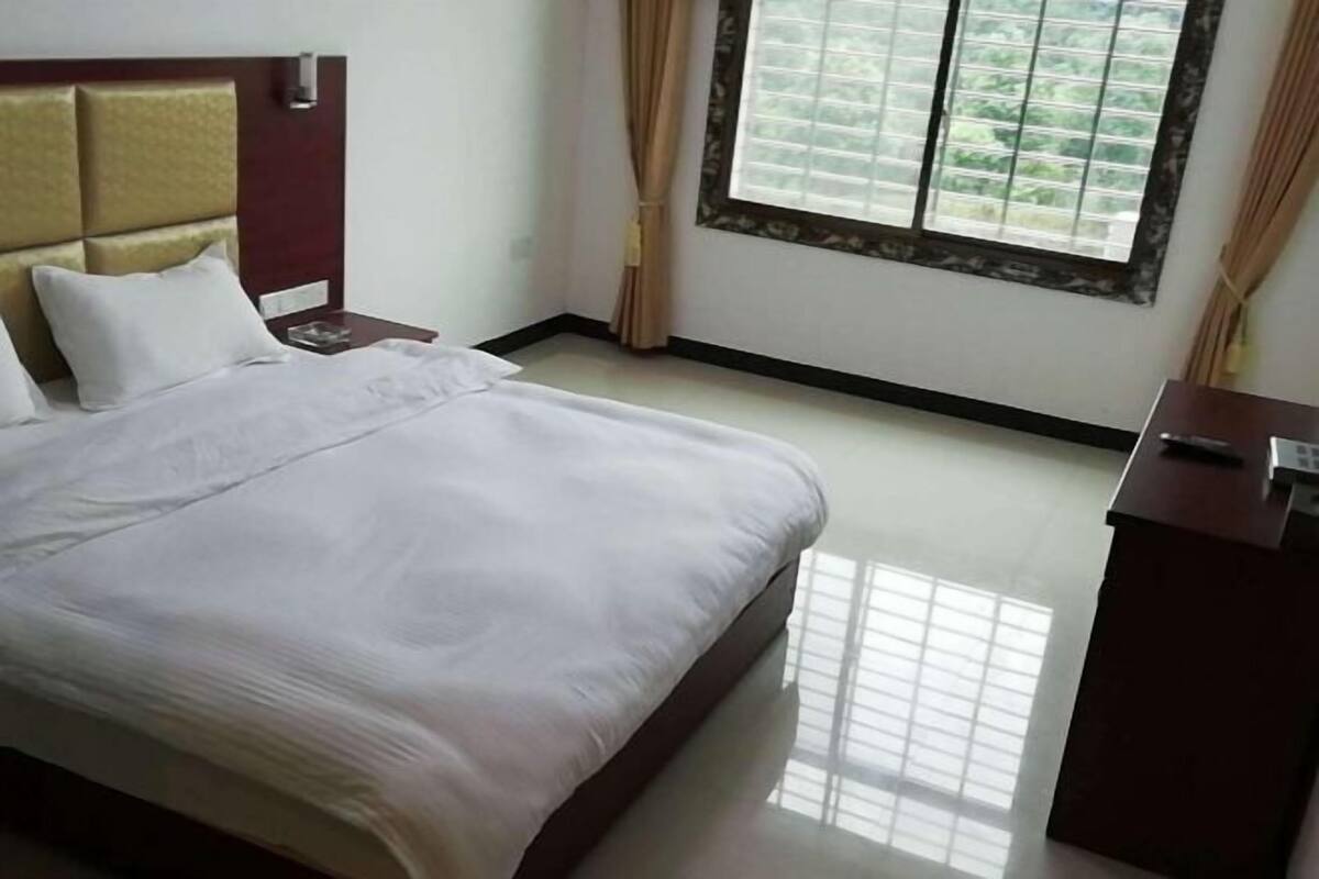 A hotel room with a bed, a nightstand, a desk, and a window with curtains.