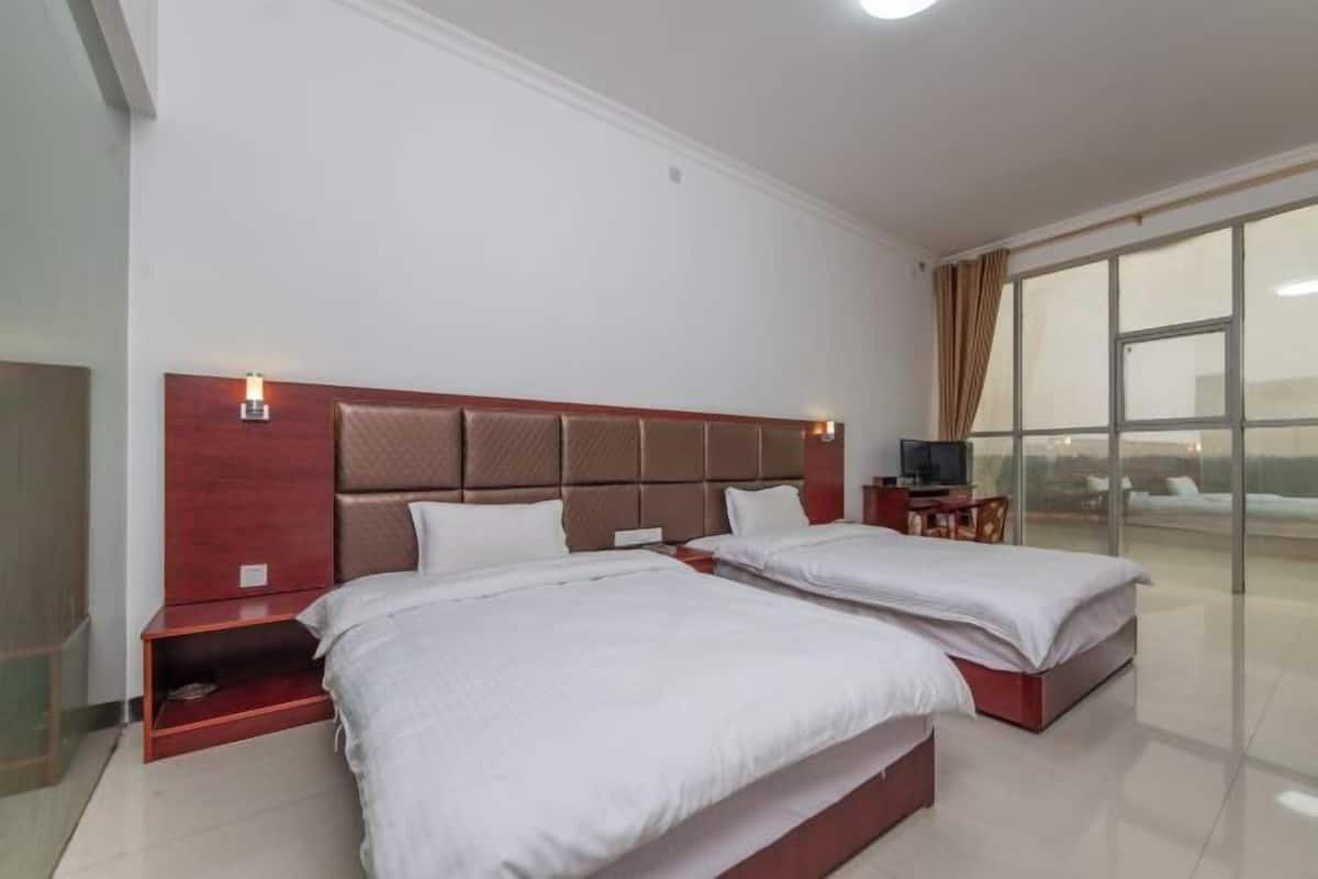 A hotel room with two beds, a TV, and a large window offering a view.