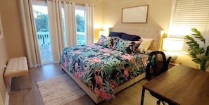 Une chambre à coucher comprenant un lit, une chaise, une table, une lampe et donnant sur l’extérieur.