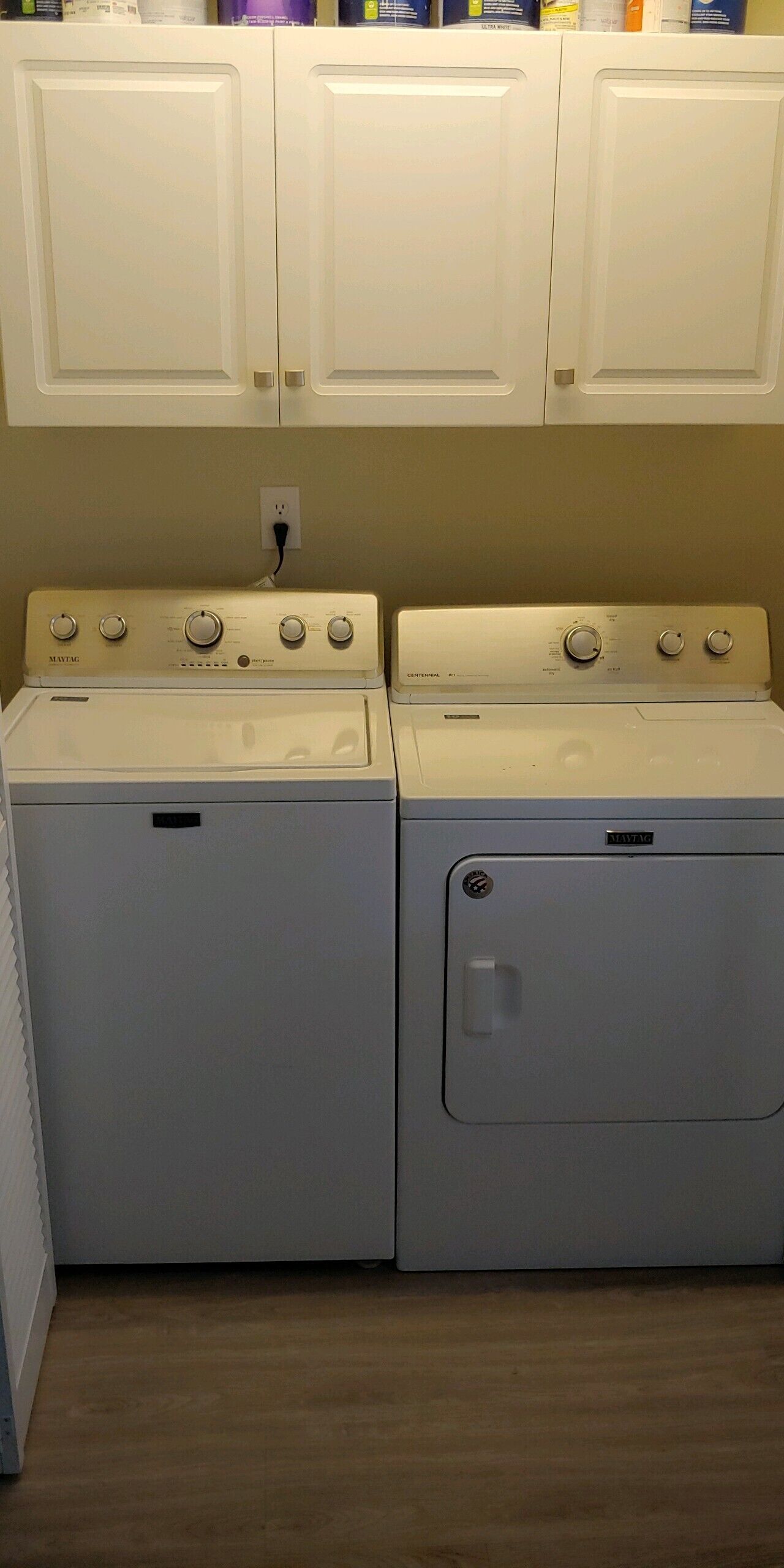A laundry room with two stacked front-loading washing machines, a white wall, and a wooden floor.