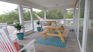 A covered porch with a wooden picnic table, potted plants, and white railings. - Palmetto Blvd just steps from the beach ! (Edisto Beach)