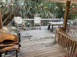 An outdoor deck with wooden furniture, a grill, and string lights.