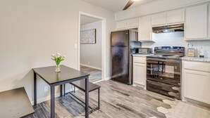 A modern kitchen with a stainless steel refrigerator, oven, and microwave. There is a dining table with a vase of flowers.
