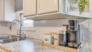 A kitchen with a granite countertop, a coffee maker, and jars labeled "coffee" and "sugar".