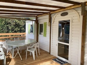 A covered outdoor area with a table and chairs, a wooden deck, and a white door with a window.