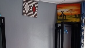 Un lit avec une couette bleue, une tête de lit en bois et un mur orné d’un tableau aux motifs géométriques et d’une scène de coucher de soleil.