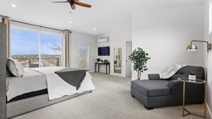 A modern bedroom with a bed, a grey sofa, a small table, a ceiling fan, and a large window with a city view. - Friends & Family Favorite! Views - Spacious - Clean (spicewood)