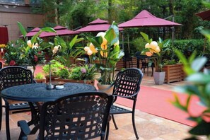 Een terras met ronde tafels en stoelen, omringd door plantenbakken en parasols.