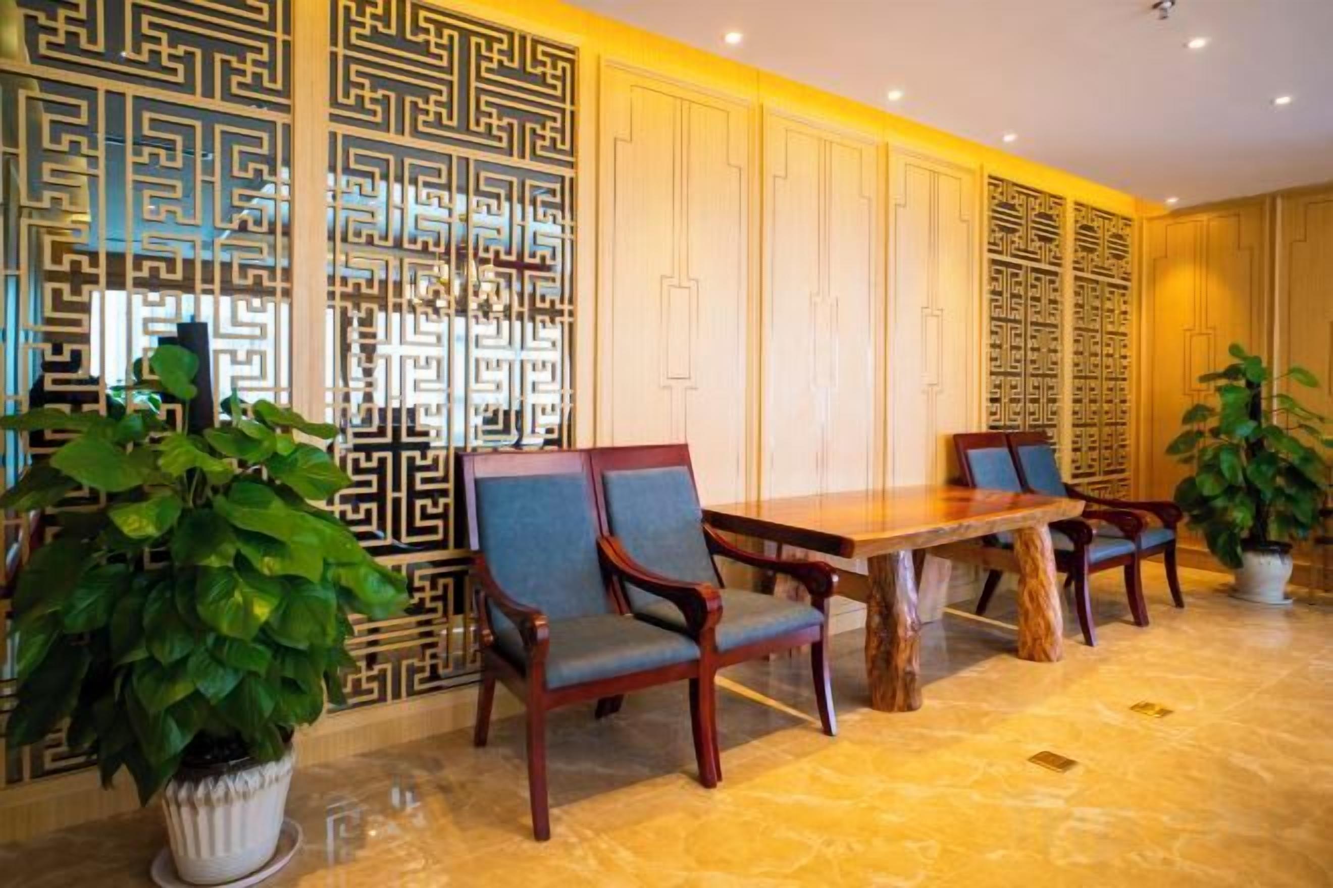 A dining area with a wooden table and chairs, a decorative wall with geometric patterns, and potted plants.