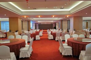 Un salón de banquetes con mesas redondas, sillas blancas, un escenario y una alfombra roja.