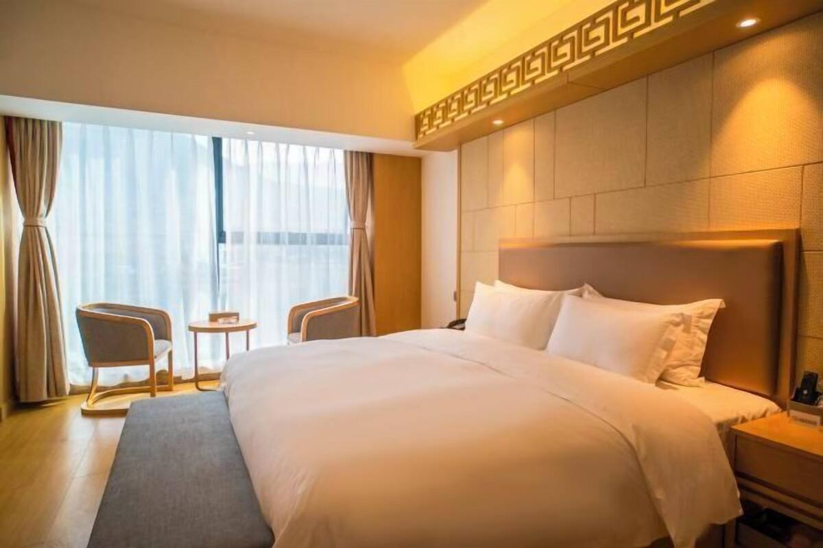 Habitación de hotel con una cama grande, una mesita de noche, una silla, una pequeña mesa y una ventana con cortinas.