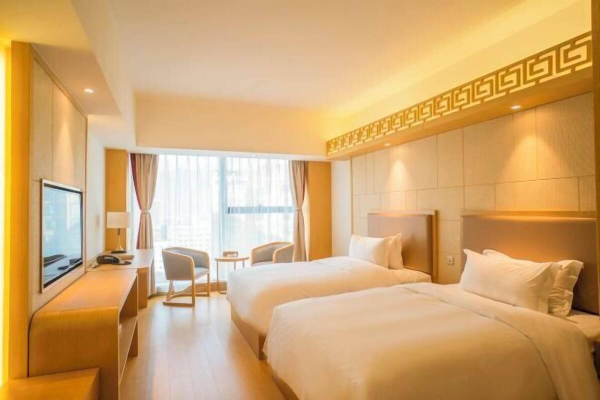 Habitación de hotel con dos camas, un escritorio con televisor, una mesita pequeña y sillas.