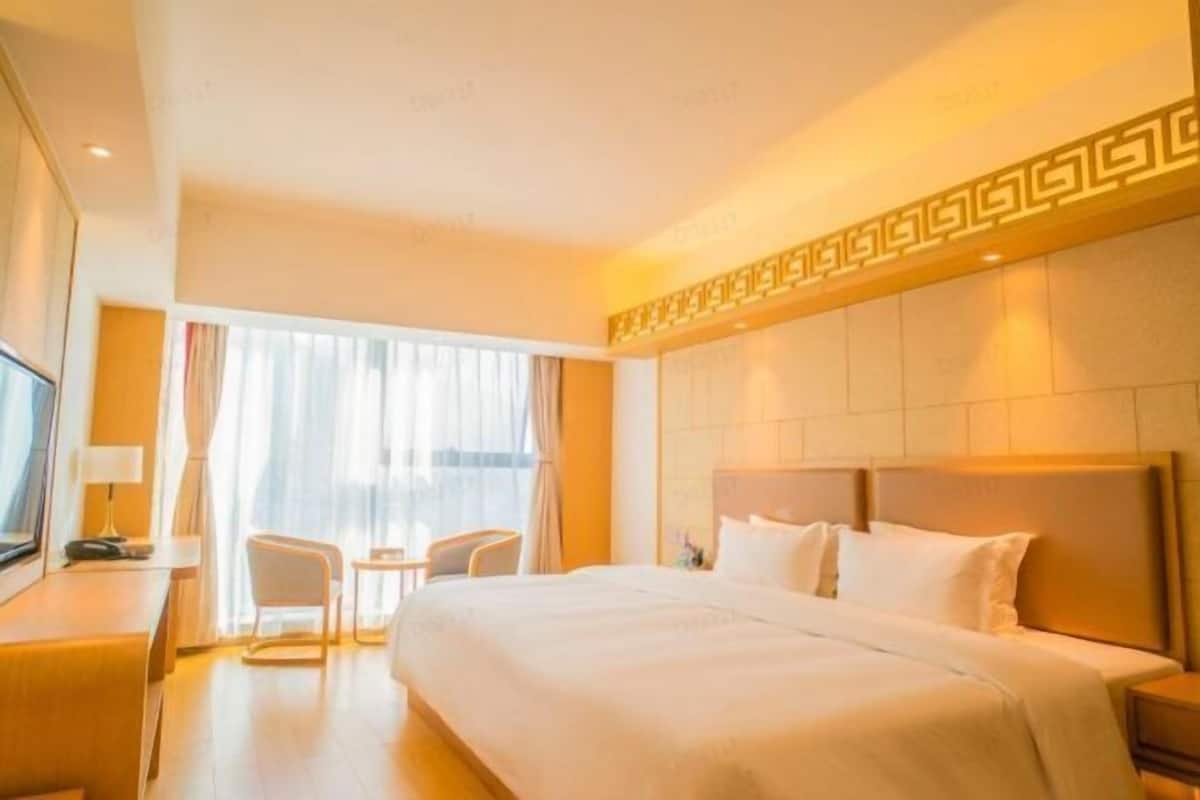 Habitación de hotel con una cama grande, un escritorio con una silla, un televisor y una ventana con cortinas.
