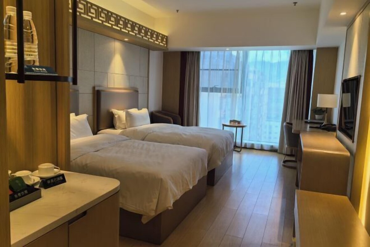 Une chambre d’hôtel avec deux lits, une table de chevet avec une lampe, une télévision et une petite table avec une plante.
