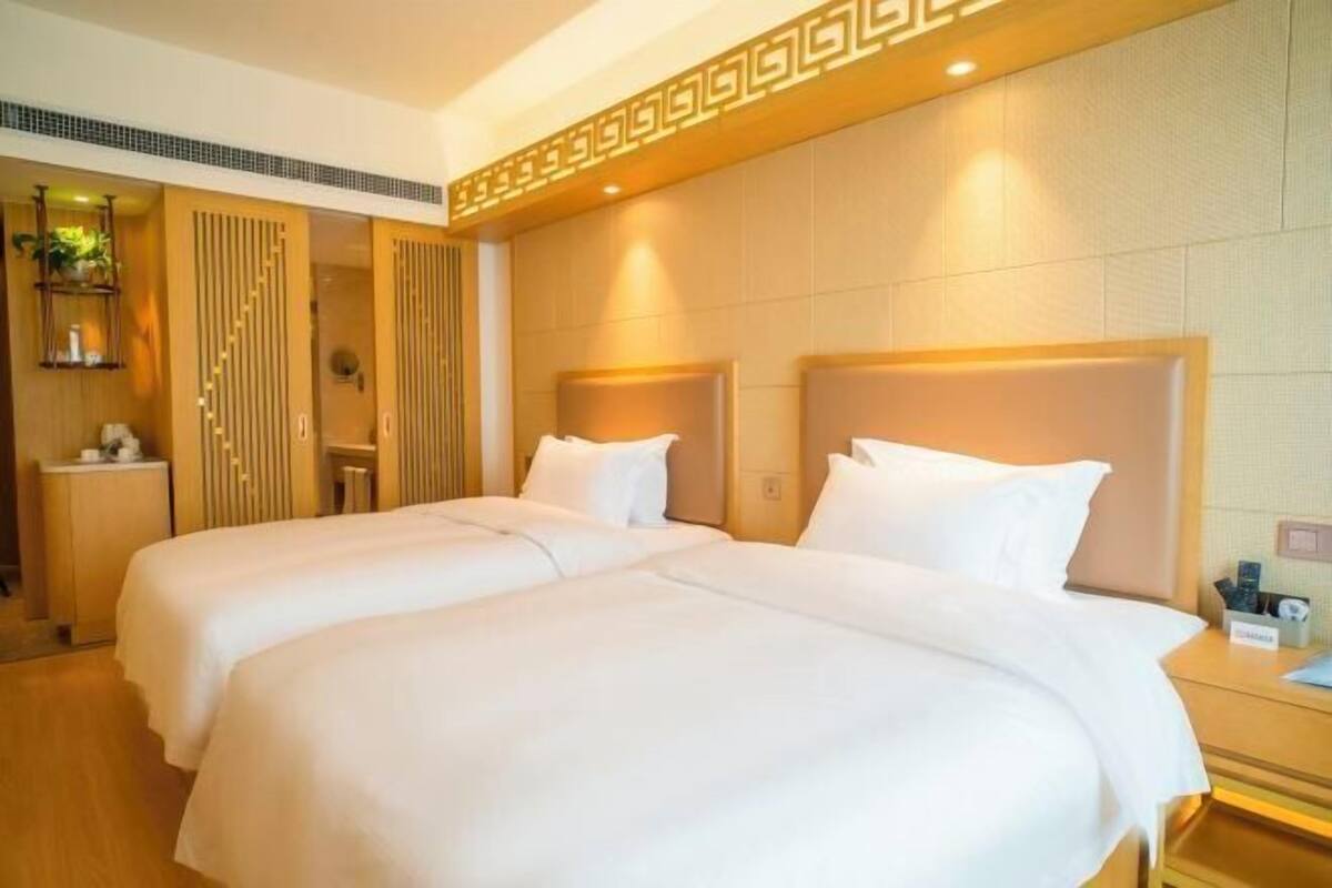 Habitación de hotel con dos camas, cabecero de madera, mesita de noche y espejo.