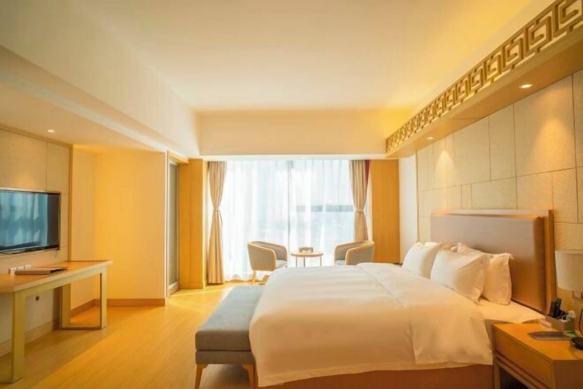 Habitación de hotel con una cama grande, televisión, escritorio y ventana con cortinas.