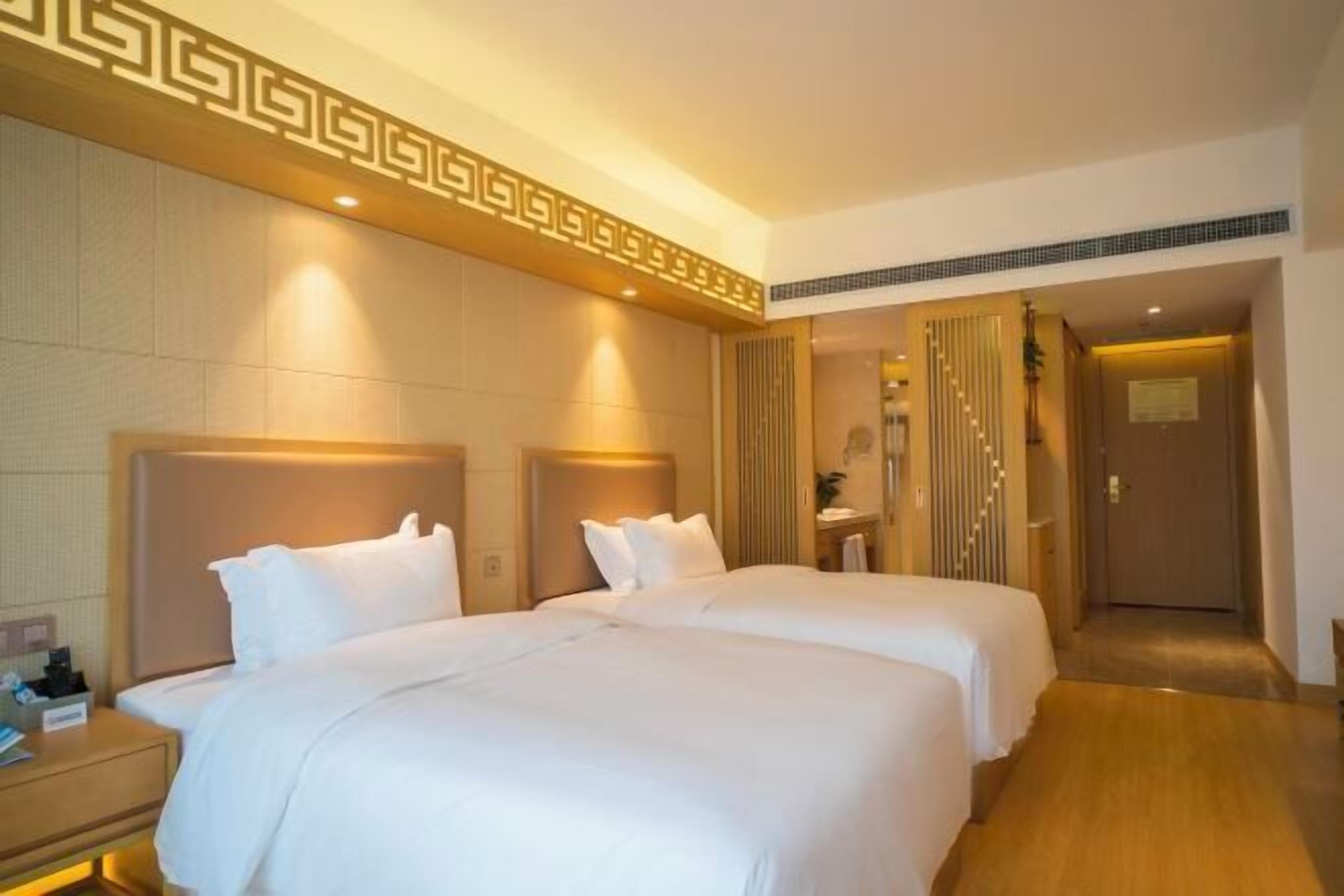 A hotel room with two beds, a bedside table, a mirror, and a door leading to a bathroom.