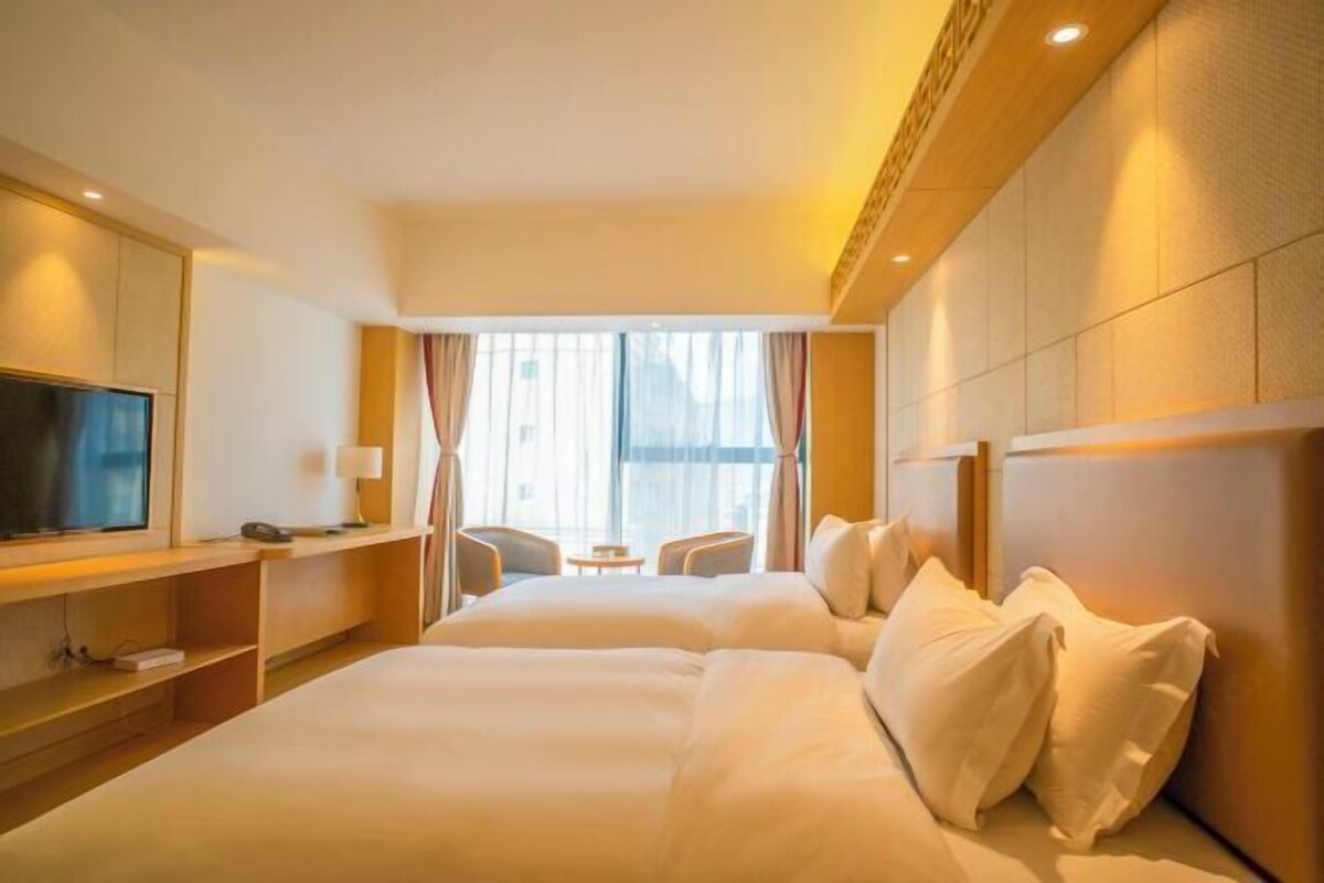 Une chambre d’hôtel avec un lit, une télévision, un bureau et une fenêtre avec des rideaux.