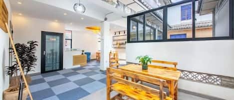 A spacious room with a wooden dining table, a potted plant, and a checkered floor.